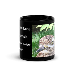 Black 11 ounce mug with graphic of a spotted thick-knee looking grumpy amongst a leafy background. In view are various common names for the Spotted Thick-knee and its scientific name.