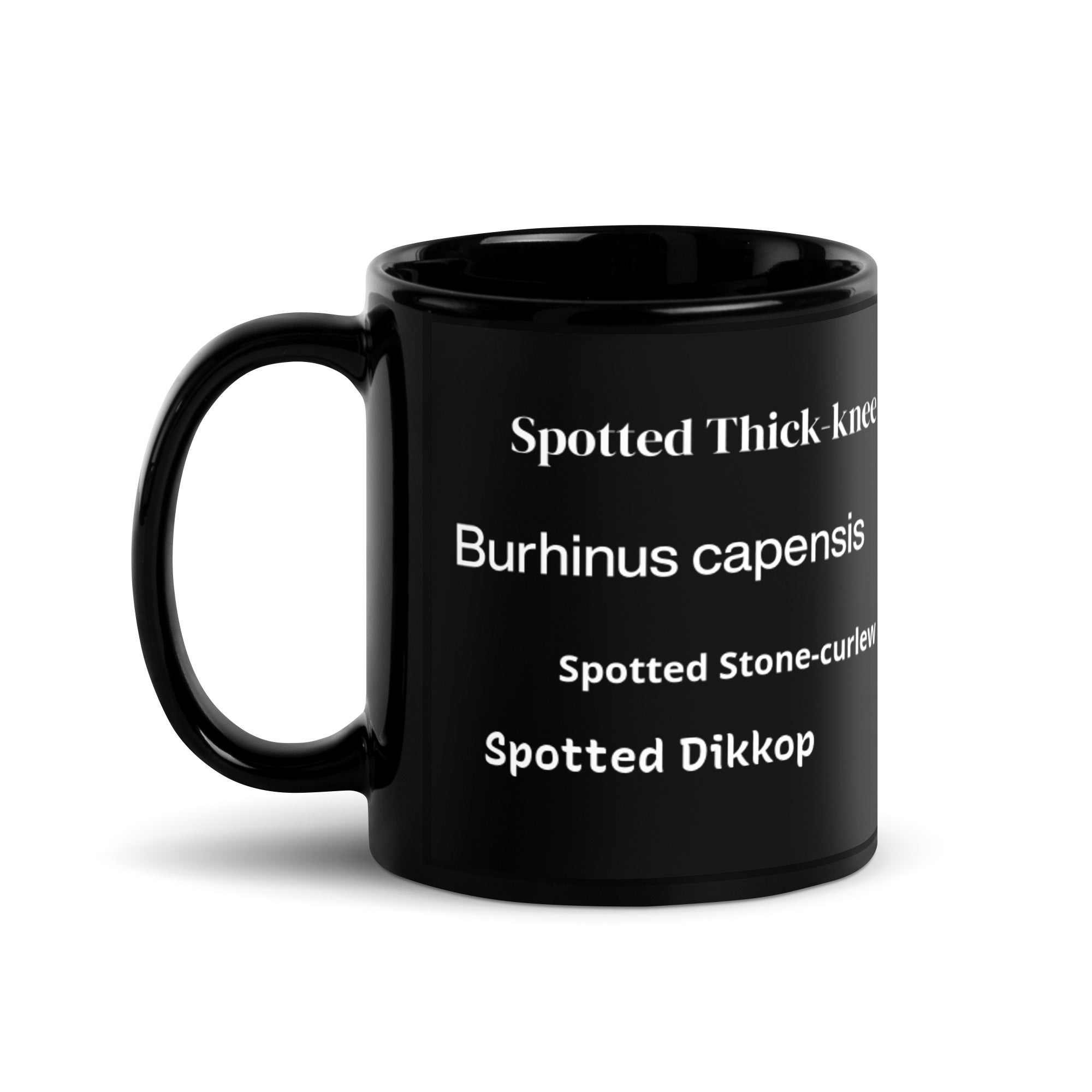 Opposite view of black 15 ounce mug with graphic of a spotted thick-knee looking grumpy amongst a leafy background. In view are the words spotted thick-knee, Burhinus capensis, Spotted Stone-curlew and Spotted Dikkop.