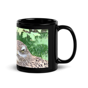 Black 11 ounce mug with graphic of a spotted thick-knee looking grumpy amongst a leafy background.