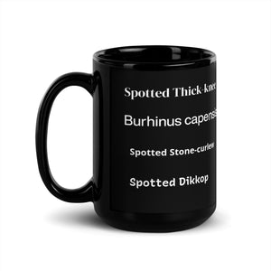 Opposite view of black 15 ounce mug with graphic of a spotted thick-knee looking grumpy amongst a leafy background. In view are the words spotted thick-knee, Burhinus capensis, Spotted Stone-curlew and Spotted Dikkop.