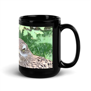 Black 15 ounce mug with graphic of a spotted thick-knee looking grumpy amongst a leafy background.