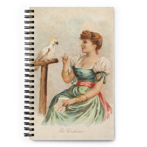 Spiral notebook with black wire binding.  The cover of the notebook has a remastered vintage art piece of a girl from the 1890s in a nice dress sitting next to a sulphur crested cockatoo parrot.