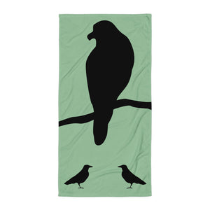 Sea green large beach towel with a large silhouette of a crow on a branch and two smaller standing crow silhouettes beneath. 