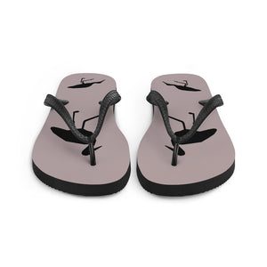 A pair of dusty purple flip-flops with black strap and a silhouette of a stork standing and smaller ones at the heel, viewed from the front.