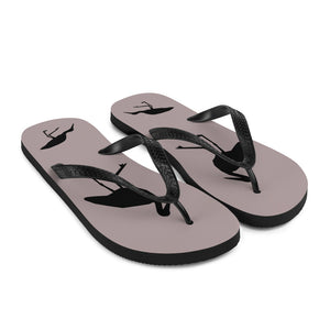 A pair of dusty purple flip-flops with black strap and a silhouette of a stork standing and smaller ones at the heel, viewed from the front right.