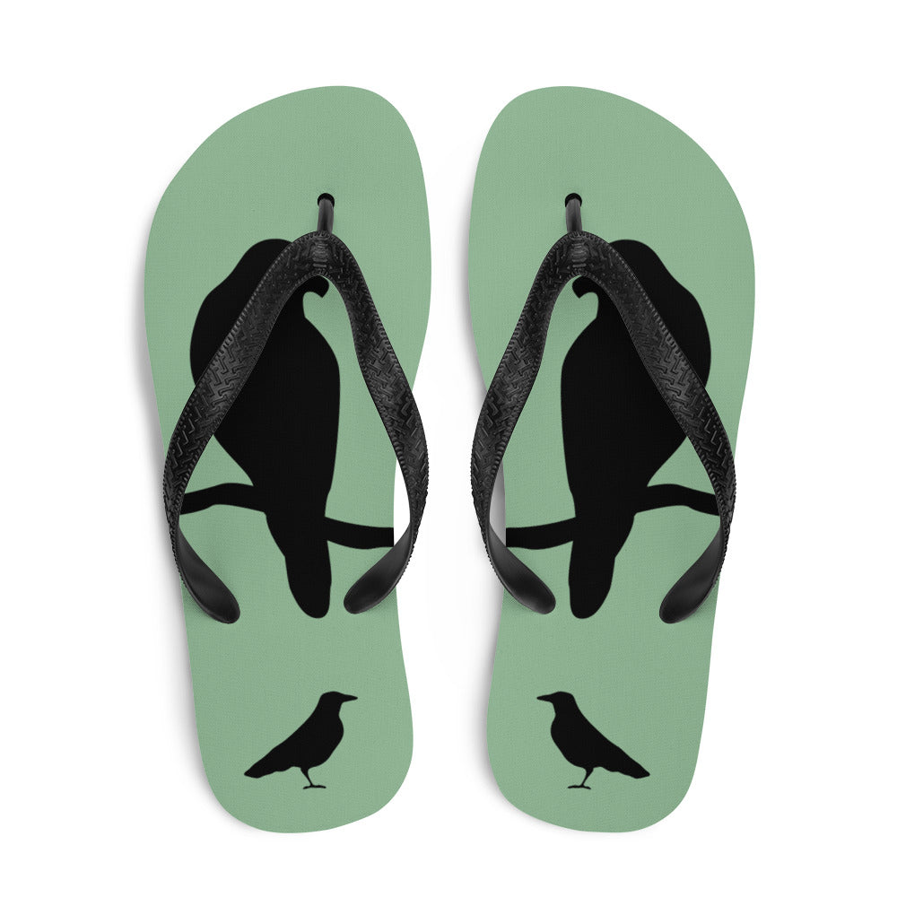 A pair of sea green flip-flops with black strap and a silhouette of a crow on a branch.