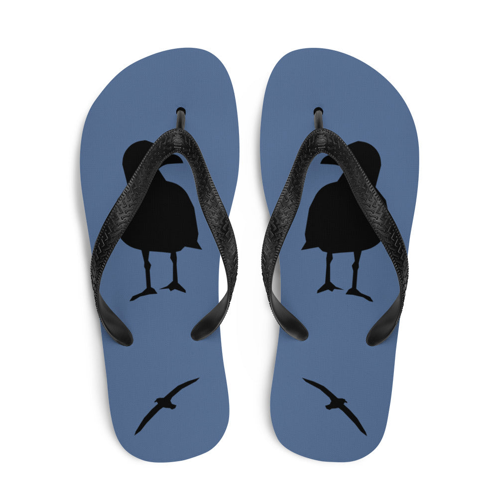 A pair of blue flip-flops with black strap and a silhouette of a seagull standing and smaller ones flying, viewed from the top down.