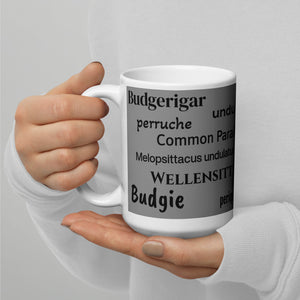 White 15 ounce coffee mug with an illustrated lifelike picture of a green and yellow budgie on a grey background next to the word budgerigar in other languages.  This view shows the words budgerigar, perruche, melopsittacus undulatus, and budgie.